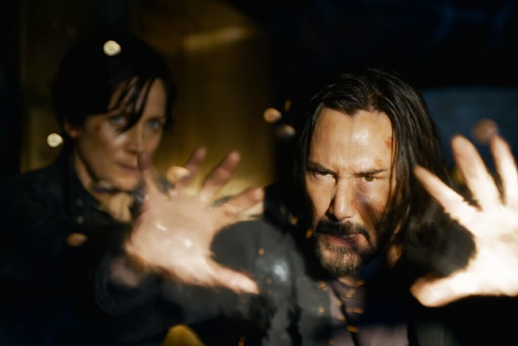 Keanu Reeves com as espalmadas usando um poder de força e Carrie-Anne Moss ao fundo